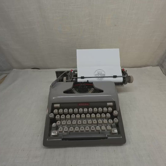 A person's hands typing on a grey typewriter.